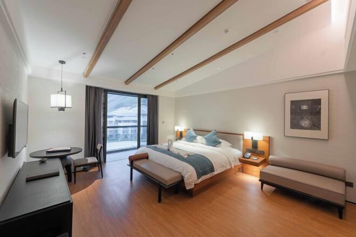 A modern hotel room with a large bed, bedside tables, a desk, and a bench.