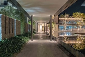 A corridor with a brick wall on one side and a glass building on the other, leading to a pool area. - Vastroam Hotel (Yongtai)