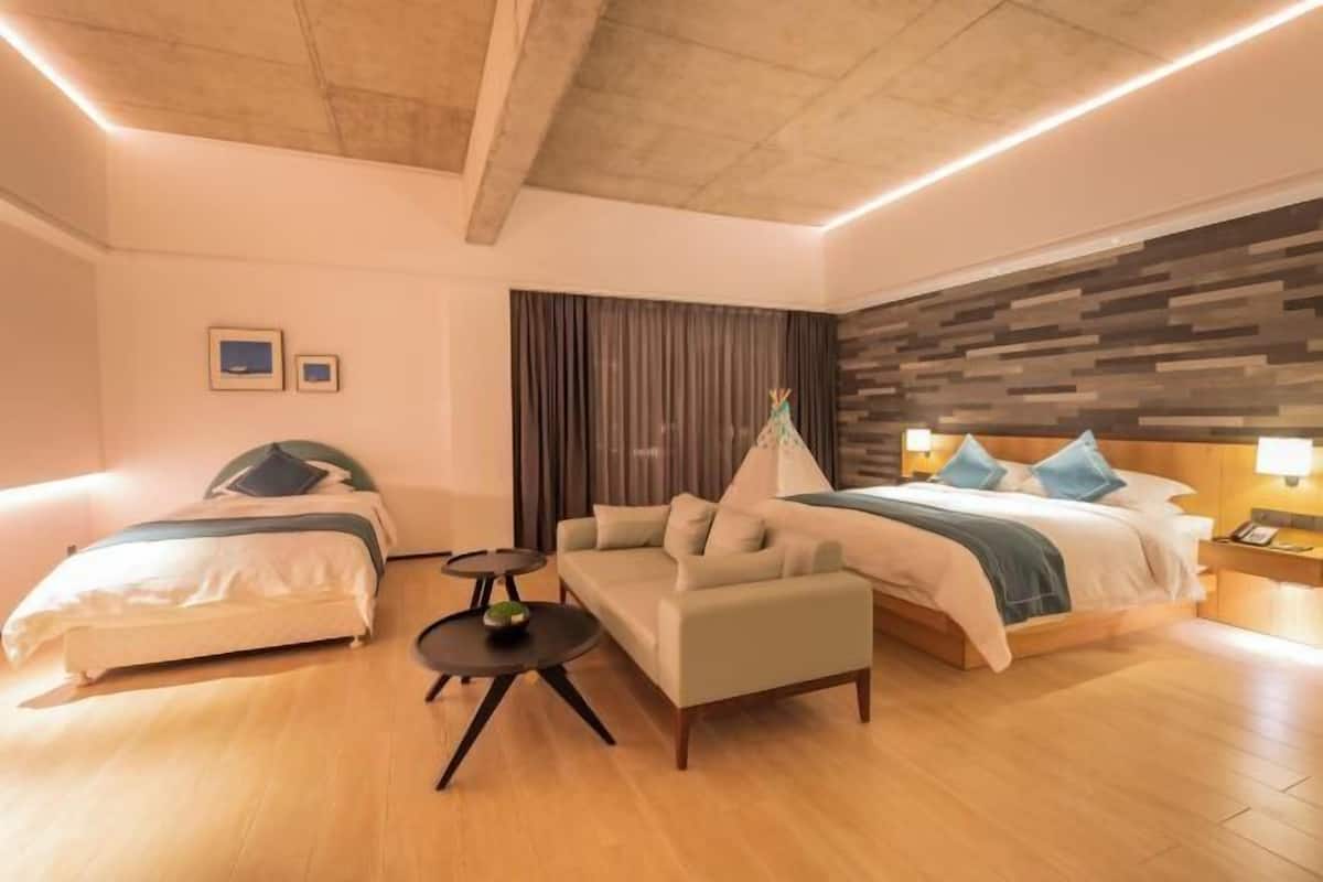 Habitación de hotel con dos camas, un sofá, una mesita y techo de madera.