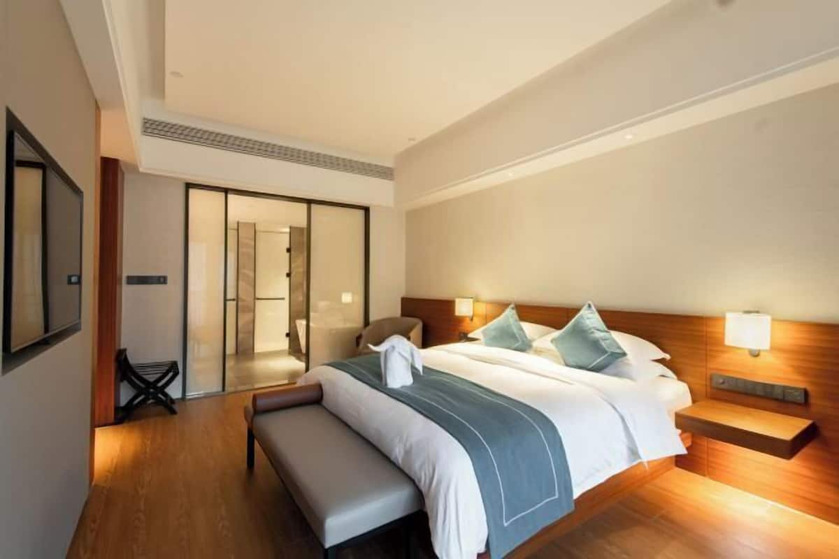 Una habitación de hotel moderna con una cama grande, un banco, una mesita de noche y una puerta corredera que da a un baño.
