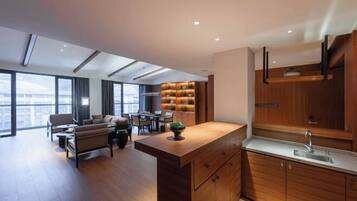 A modern kitchen with wooden cabinets and a central island, a dining area with a sofa and chairs, and large windows offering a city view.
