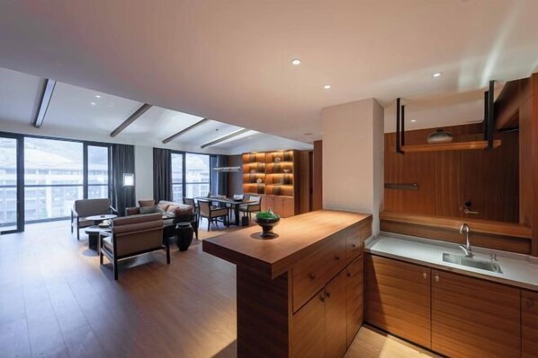 A modern kitchen with wooden cabinets and a central island, a dining area with a sofa and chairs, and large windows offering a city view. - Vastroam Hotel (Yongtai)
