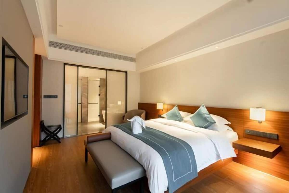 Una habitación de hotel moderna con una cama grande, un banco, un escritorio y una puerta corredera que da al baño.