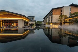 A modern hotel with a reflective pool, a lounge area, and a building with a unique roof design. - Vastroam Hotel (Yongtai)