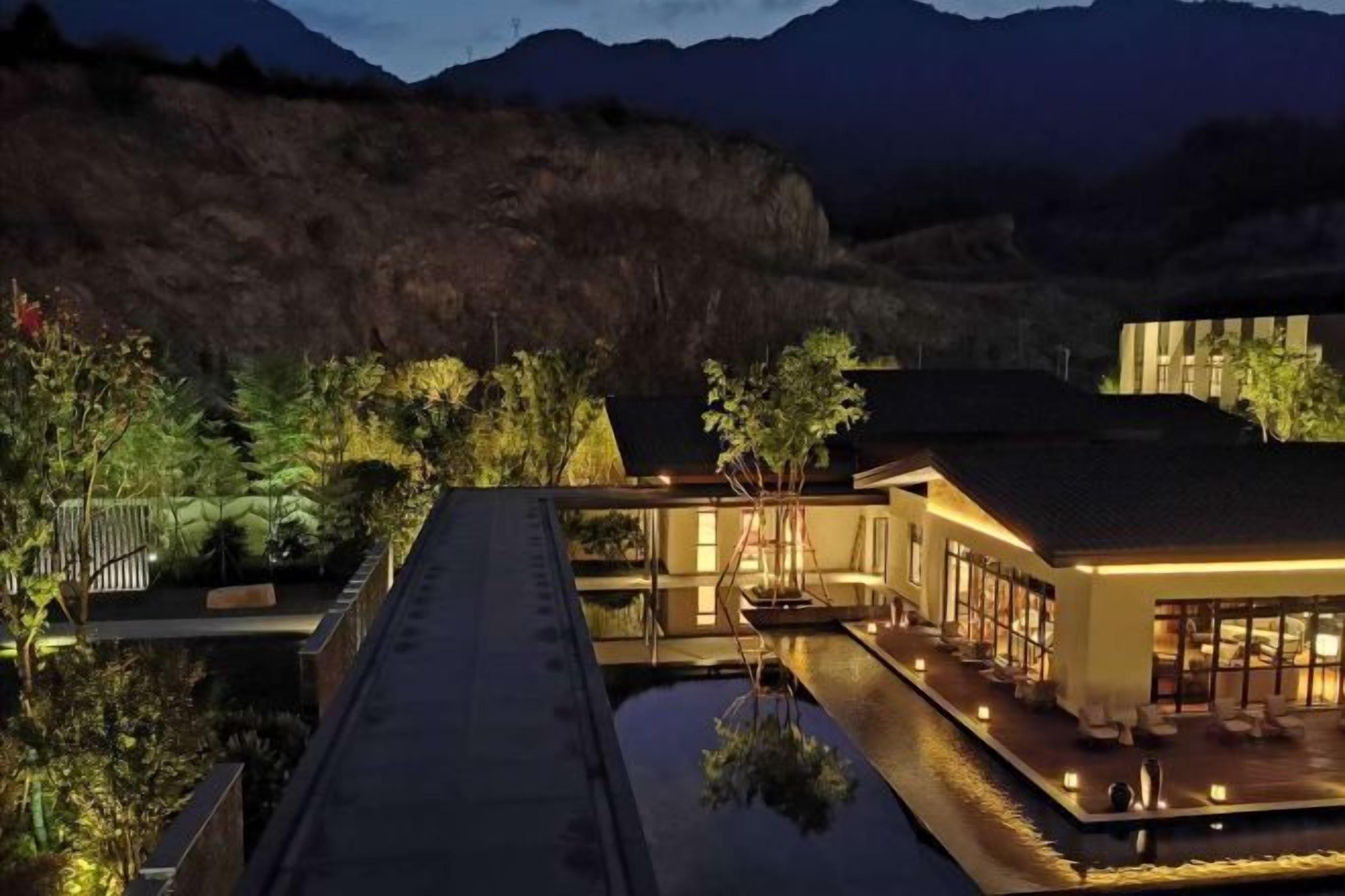 Un hotel moderno con piscina en la azotea, rodeado de exuberante vegetación y montañas al fondo.