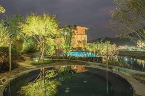 A nighttime view of a resort with a swimming pool, trees, and a building with a pool in the background. - Vastroam Hotel (Yongtai)