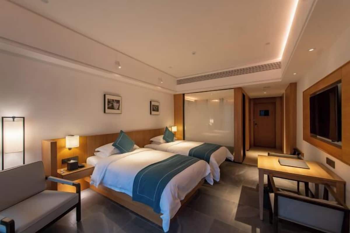 Habitación de hotel con dos camas, un escritorio, una silla, un televisor y una mesita de noche con lámpara.