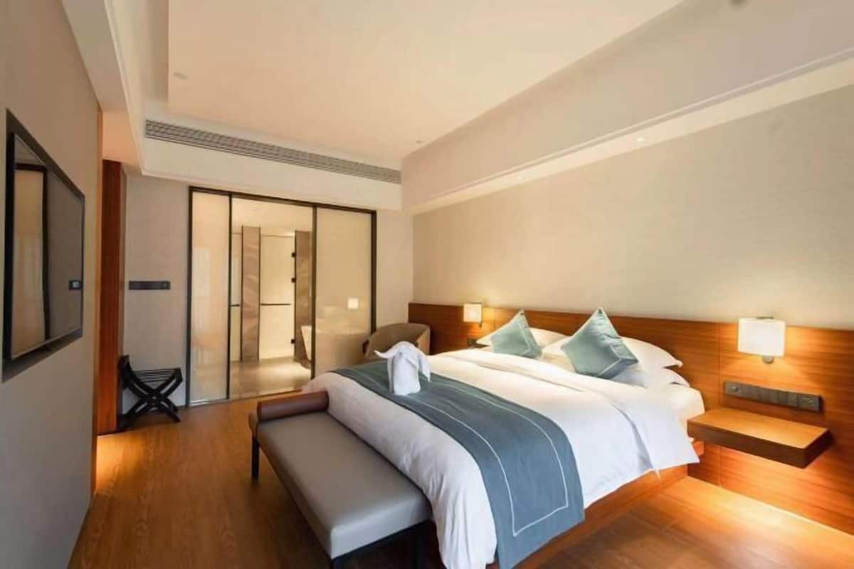 Una habitación de hotel moderna con una cama grande, un banco, una mesita de noche y una puerta corredera que da al baño.