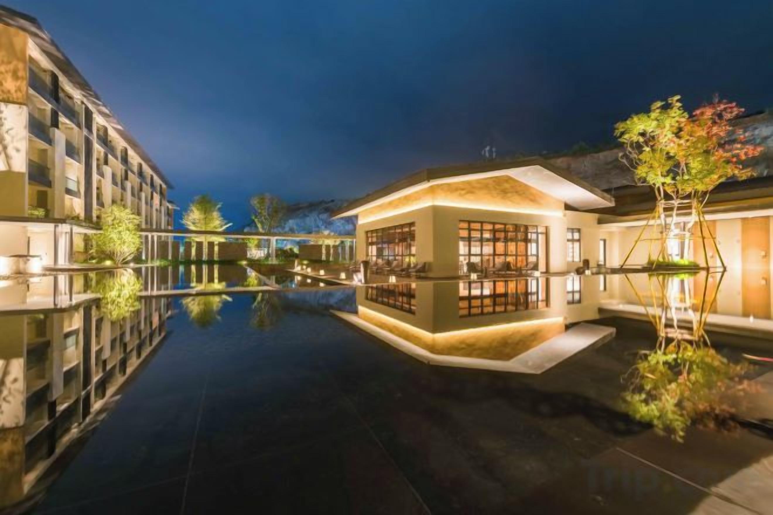 A hotel with a reflective pool, a building with large windows, and a tree with autumn foliage.