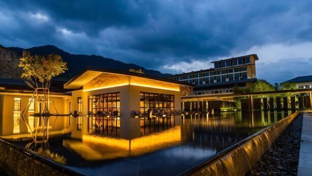 Ein modernes Hotel mit Pool, der Gebäude und Berge im Hintergrund spiegelt.