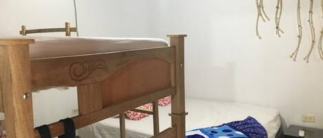 A bunk bed with a wooden headboard, a single bed with a patterned blanket, a wall-mounted air conditioner, and a small bedside table with a lamp.