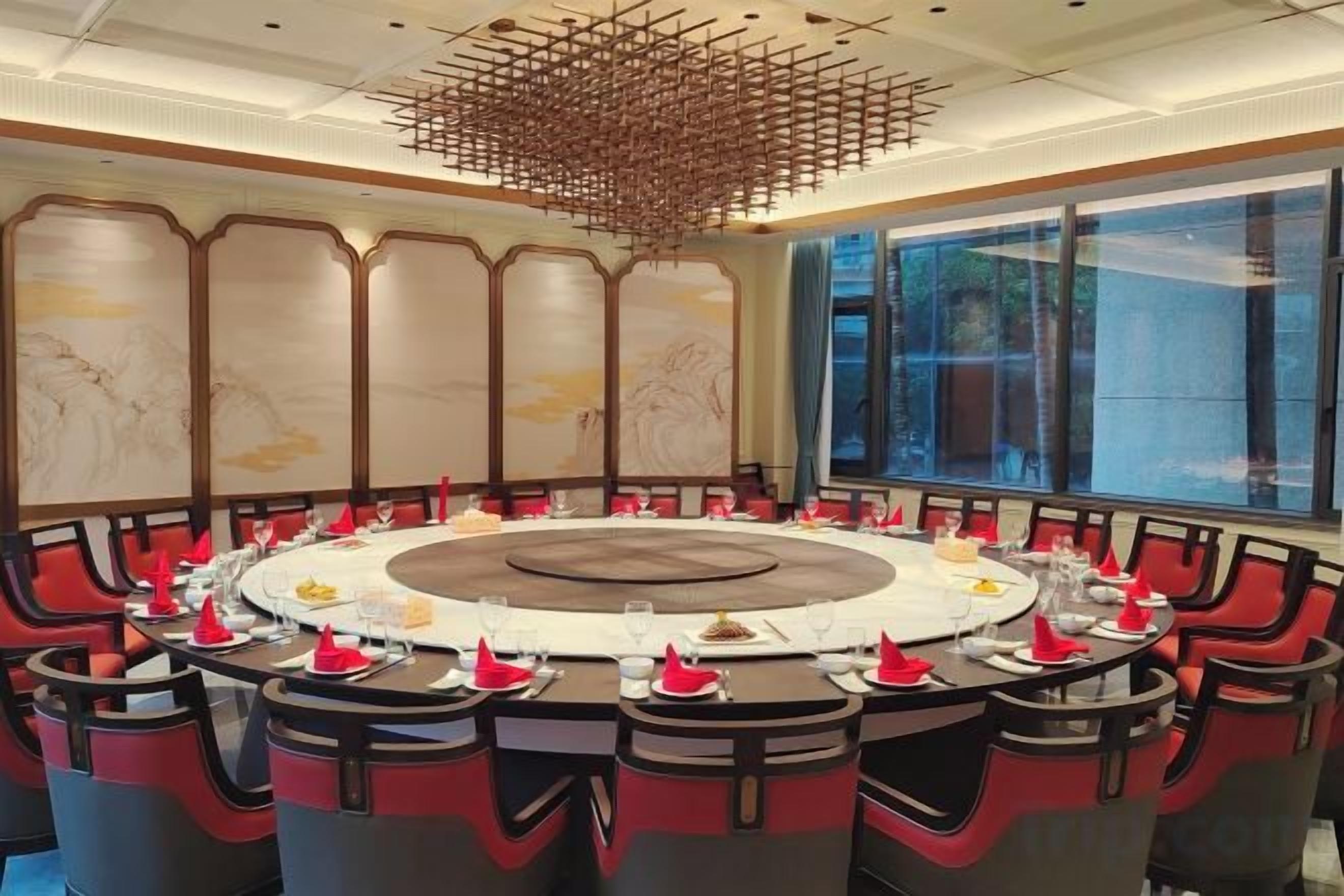 A conference room with a round table, red and black chairs, and a decorative ceiling light fixture.