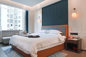A hotel room with a large bed, a bedside table, a chair, a window, and a view of a building.