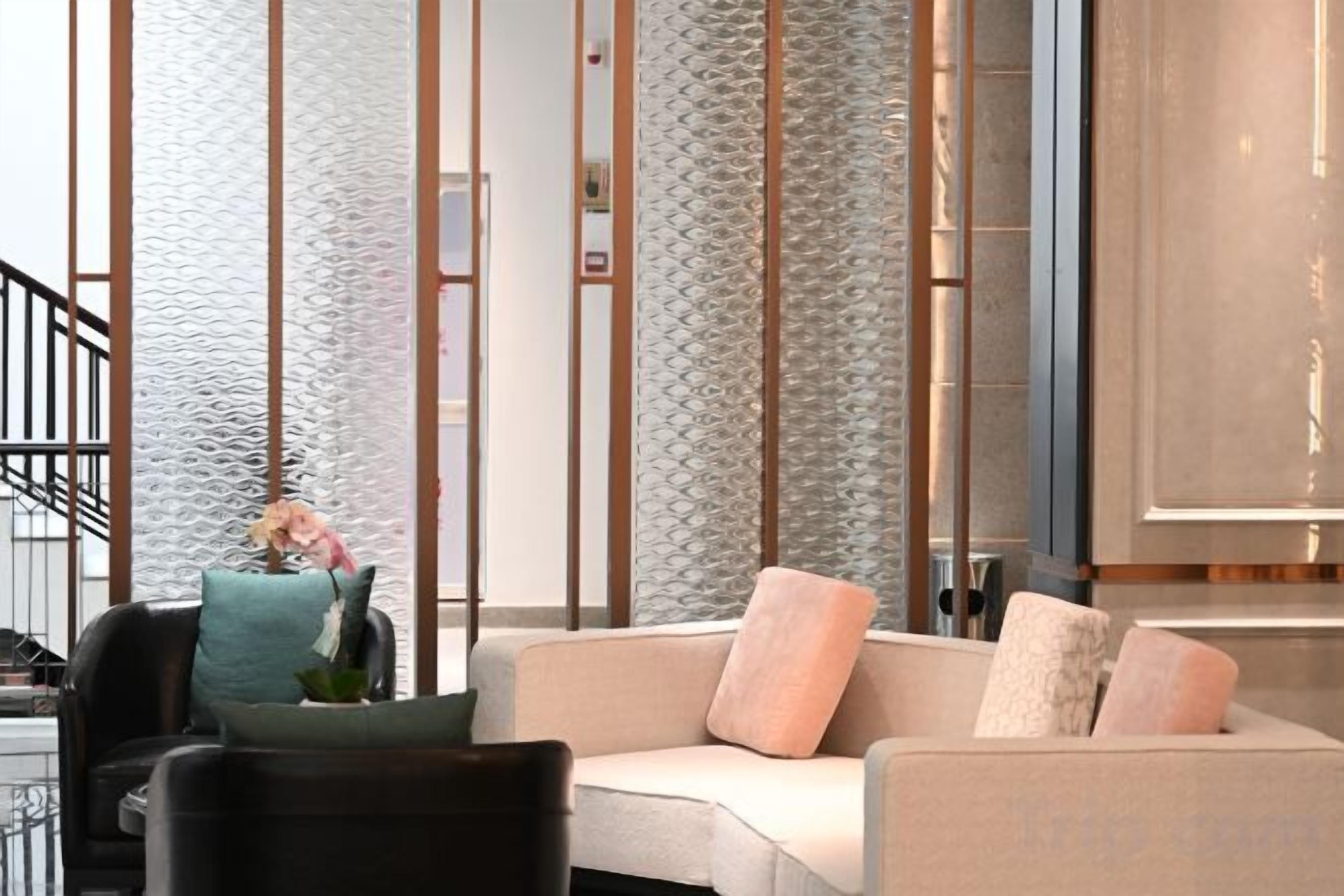 A modern interior with a sofa and chairs, a staircase, and a textured wall.