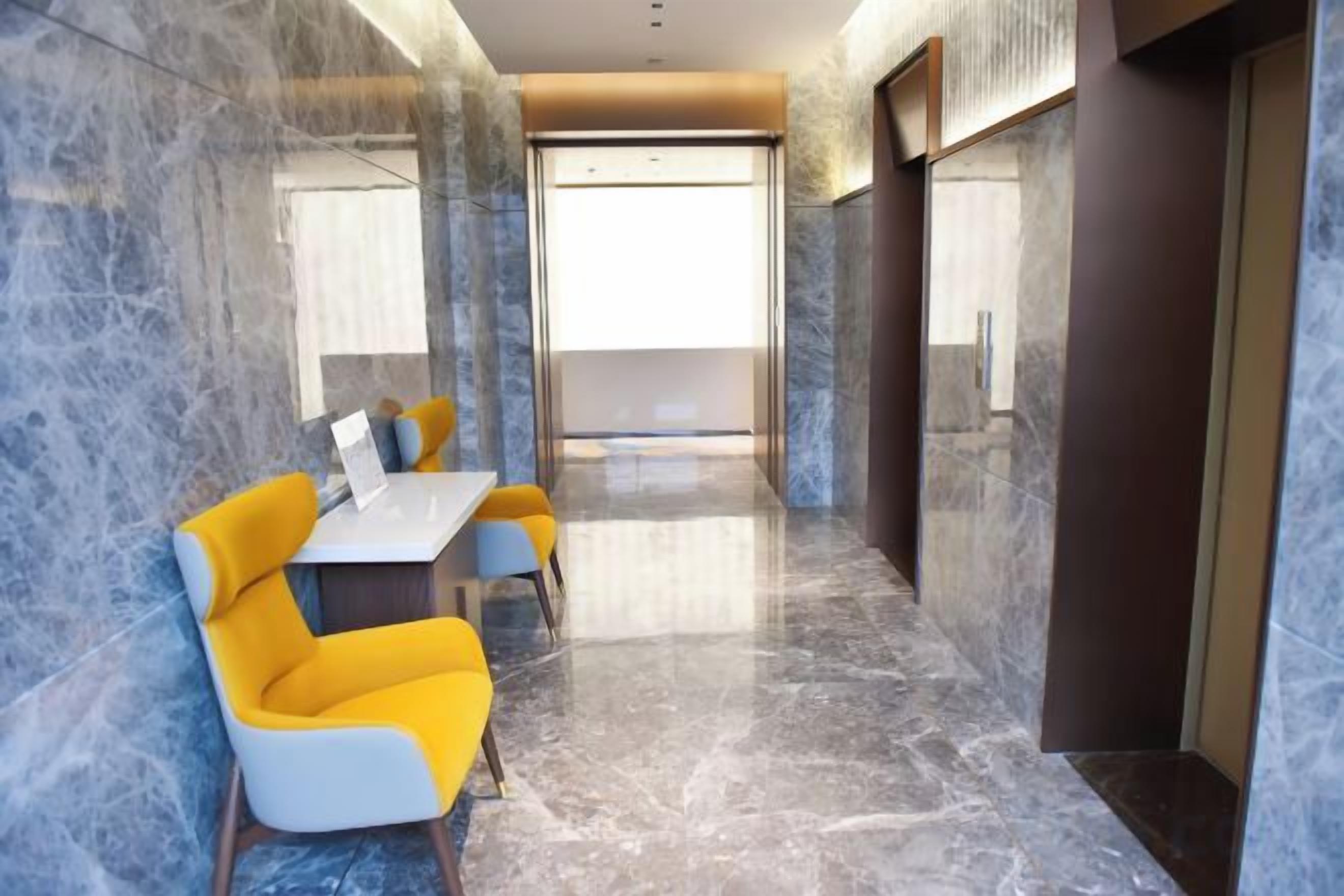 A modern hotel lobby with a marble floor, a reception desk, and bright yellow chairs.