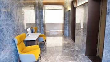 A modern hotel lobby with a marble floor, a reception desk, and bright yellow chairs.