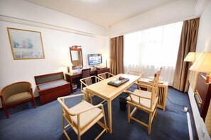 Een hotelkamer met een eettafel, stoelen, een televisie, een bureau en een raam met gordijnen.