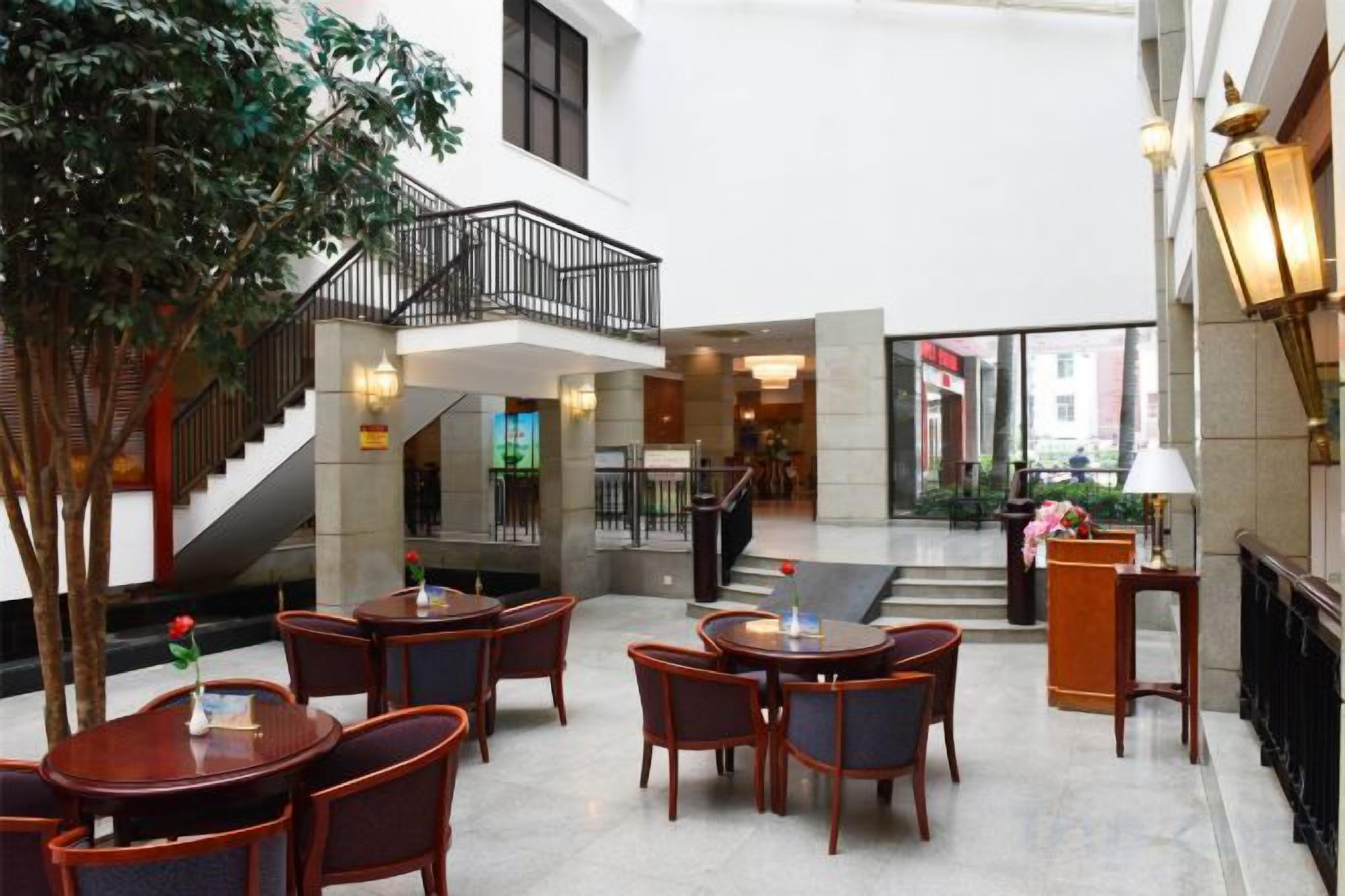 A hotel lobby with a central staircase, multiple seating areas, and a large indoor plant.