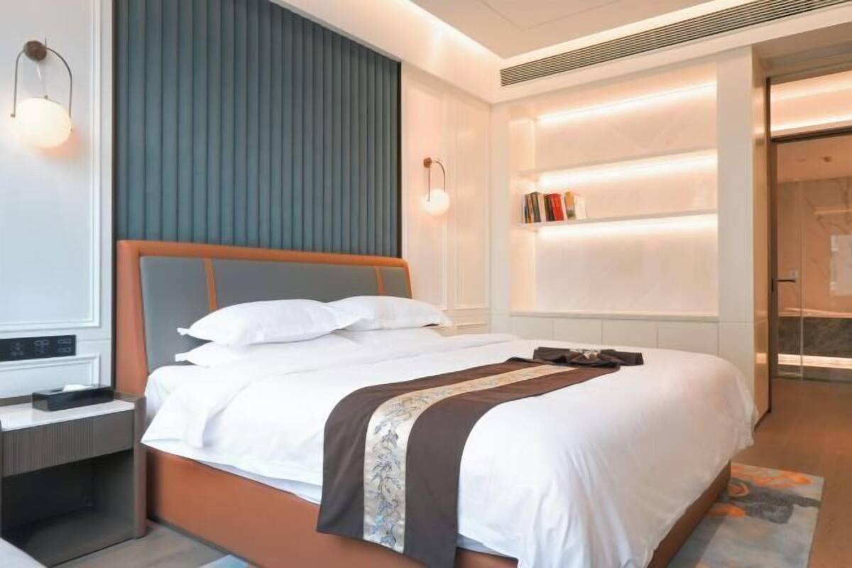 Une chambre d’hôtel moderne dotée d’un grand lit, de tables de chevet, d’une bibliothèque intégrée et d’une porte coulissante donnant accès à la salle de bain.