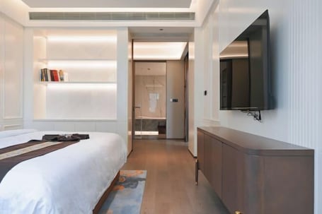 A hotel room with a bed, bedside table, TV, and a walk-in closet.. Minqing Qiyuan Hotel