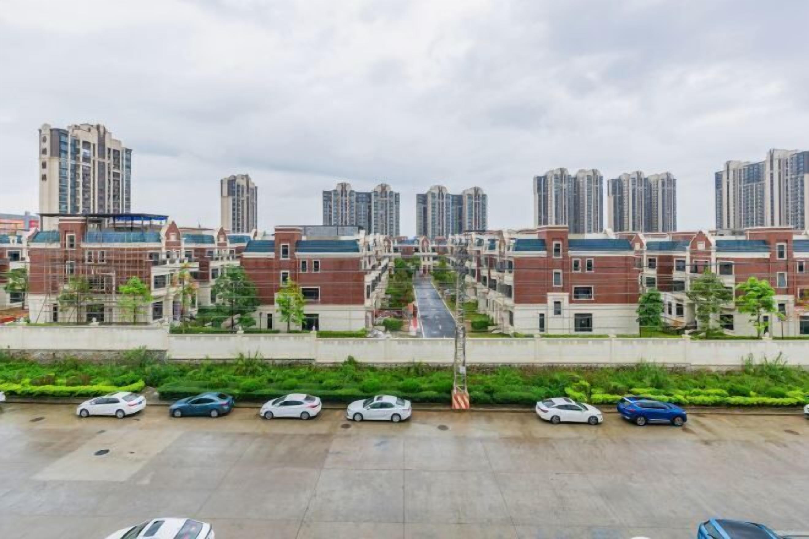 Zona residencial com edifícios altos, um estacionamento com vários carros e céu claro.