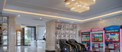 A hotel lobby with a reception desk, massage chairs, and a chandelier.