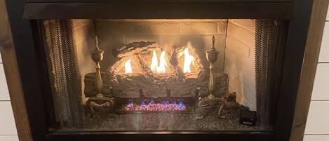 A fireplace with a black frame, logs, and a glass front.