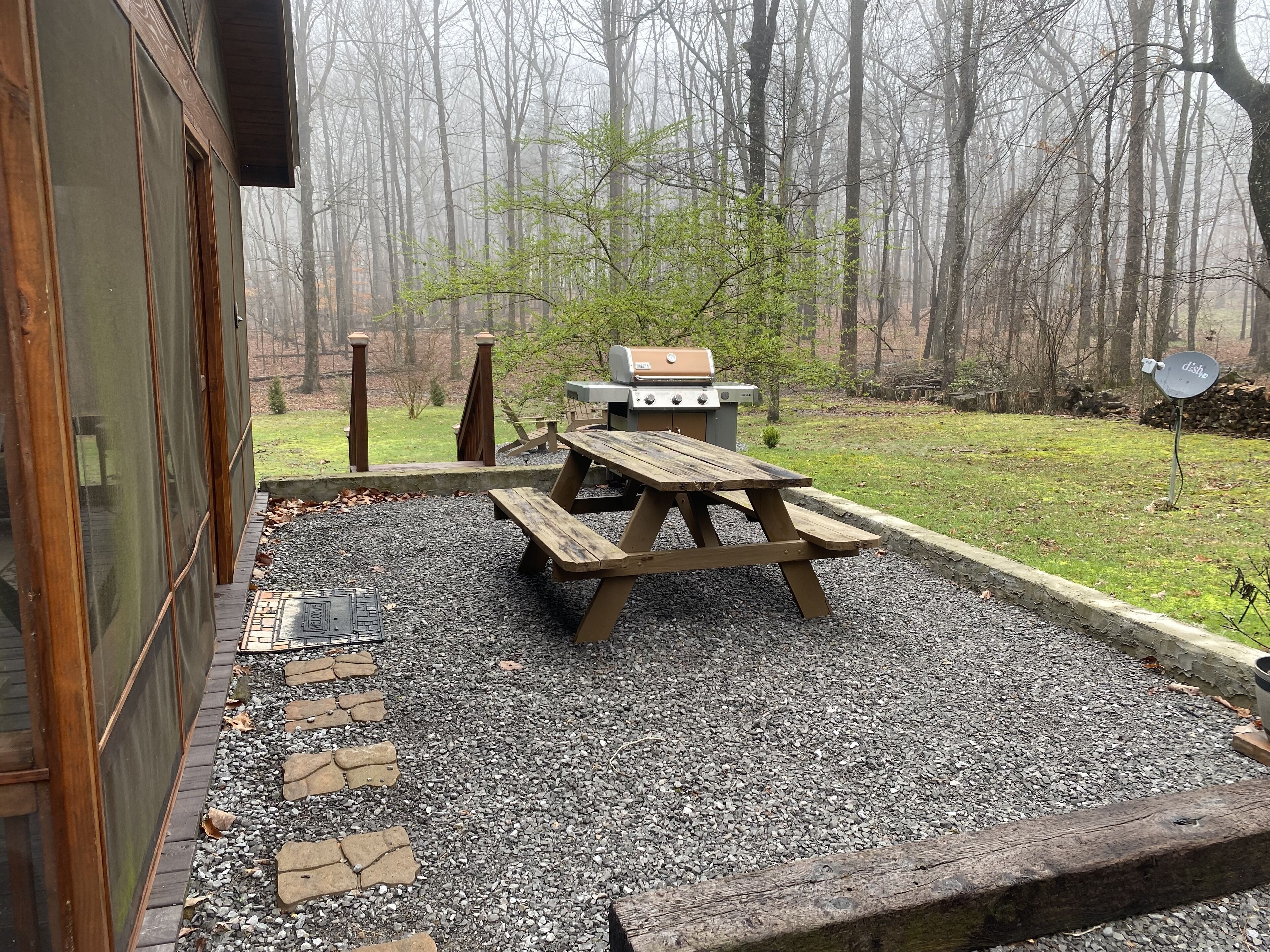 An outdoor patio with a grill and picnic table, surrounded by a gravel area and a stone border.