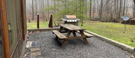 An outdoor patio with a grill and picnic table, surrounded by a gravel area and a stone border.