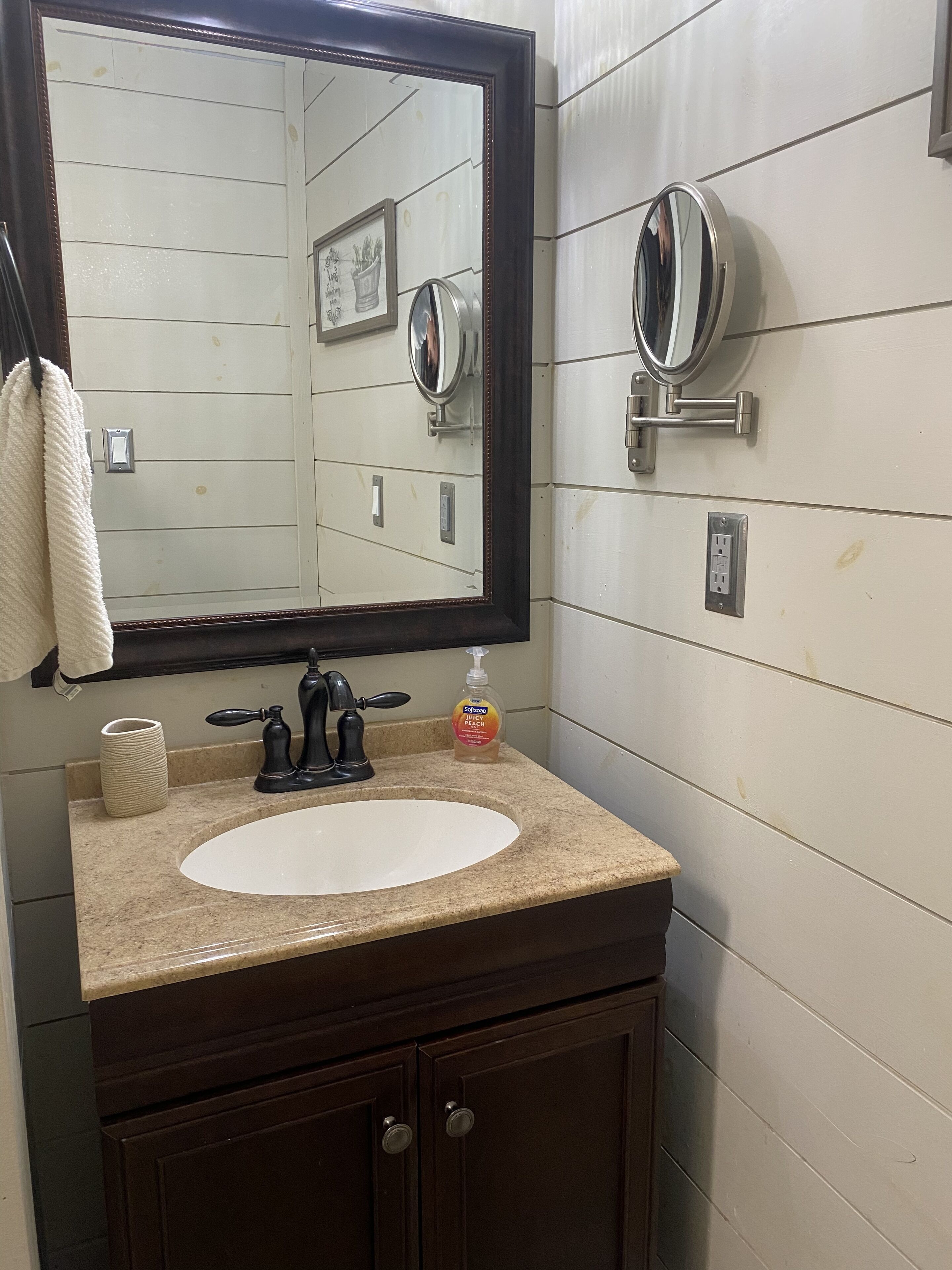 A bathroom with a white sink, dark wooden vanity, a large mirror, and a wall-mounted light fixture.