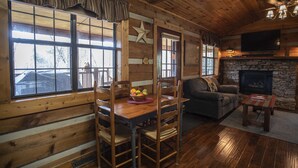 L’intérieur chaleureux d’un chalet avec une table à manger en bois, des chaises, un canapé et une cheminée.