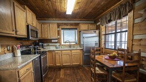 Une cuisine rustique avec des meubles en bois, un réfrigérateur en acier inoxydable, un four à micro-ondes et un coin repas comprenant une table et des chaises en bois.