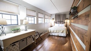 Une chambre à coucher avec un lit, des tables de chevet, un bureau et une fenêtre avec des stores.
