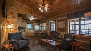 L’intérieur chaleureux d’un chalet avec des murs en bois, un coin repas, une cuisine et un salon comprenant deux canapés et une table basse.