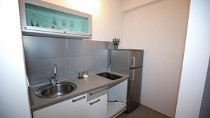 A compact kitchen with a stainless steel sink, a built-in microwave, a refrigerator, and a small potted plant on the countertop. - Unique Apartment Platnik (Skopje)