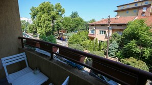 A balcony with a white bench and a table, overlooking a street with parked cars and buildings. - Unique Apartment Platnik (Skopje)