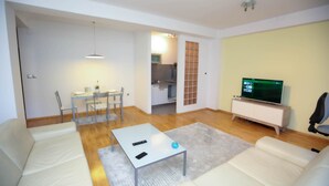 A modern living room with a sofa, a coffee table, a TV, and a dining area with chairs and a table. - Unique Apartment Platnik (Skopje)