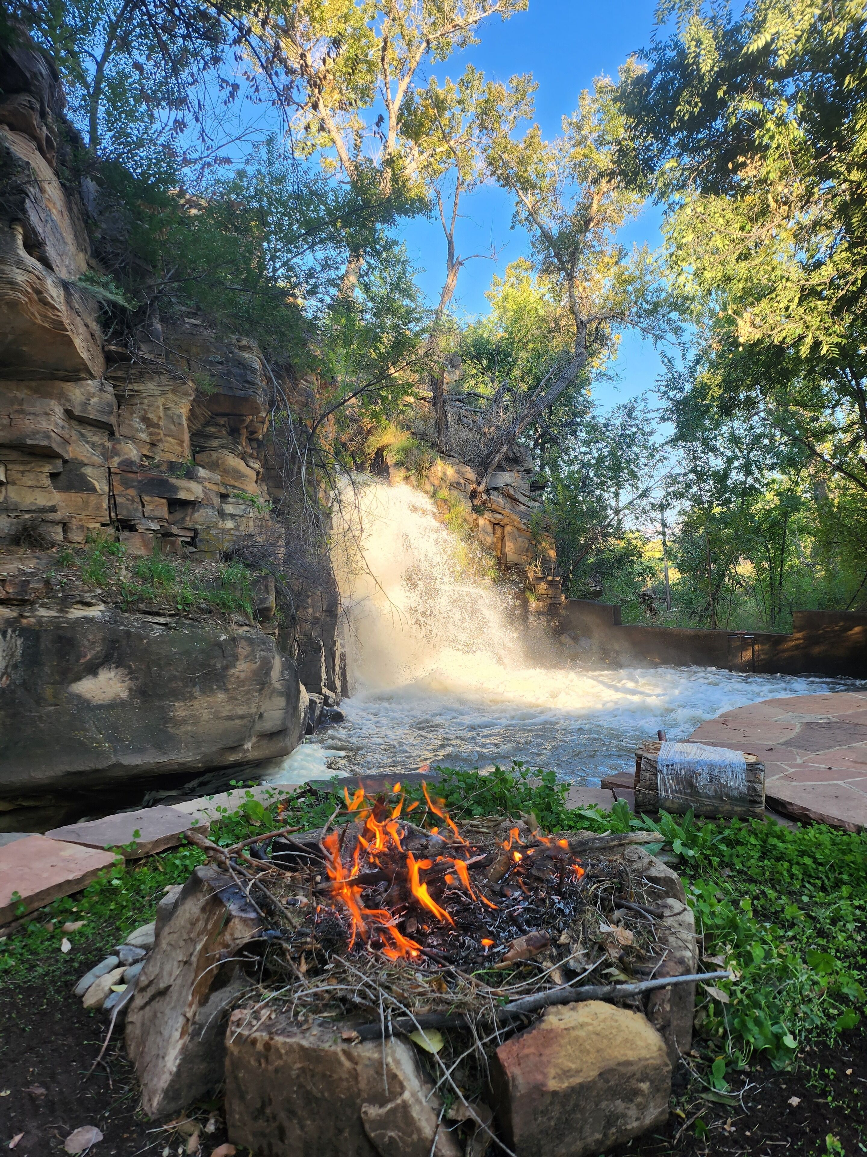 A natural setting with a rocky cliff, a flowing river, and a campfire.