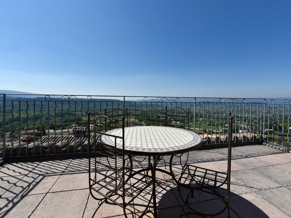 A round metal table with a tiled top, surrounded by a metal fence with a view of a green landscape.