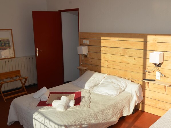 A neatly made bed with white linens and a red accent pillow, a wooden bench, and a wooden-framed door. - Caesar Panoramic Hotel Restaurant (Bonnieux)