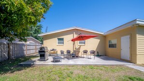 A backyard with a barbecue grill, outdoor seating, and a red umbrella.