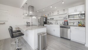 A modern kitchen with white cabinetry, stainless steel appliances, and a central island with bar stools.