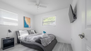 A modern bedroom with a curved bed, a ceiling fan, a mounted TV, and a nightstand with a lamp.