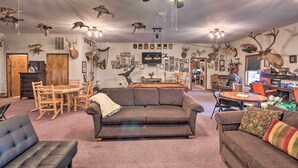 A living room with a brown sofa, a black leather couch, and a dining area with a wooden table and chairs. - Pheasant Game Farm Missouri Vacation Rental! (Braymer)