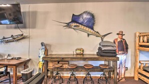 A bar area with a wooden table, stools, and a mounted fish decoration. - Pheasant Game Farm Missouri Vacation Rental! (Braymer)