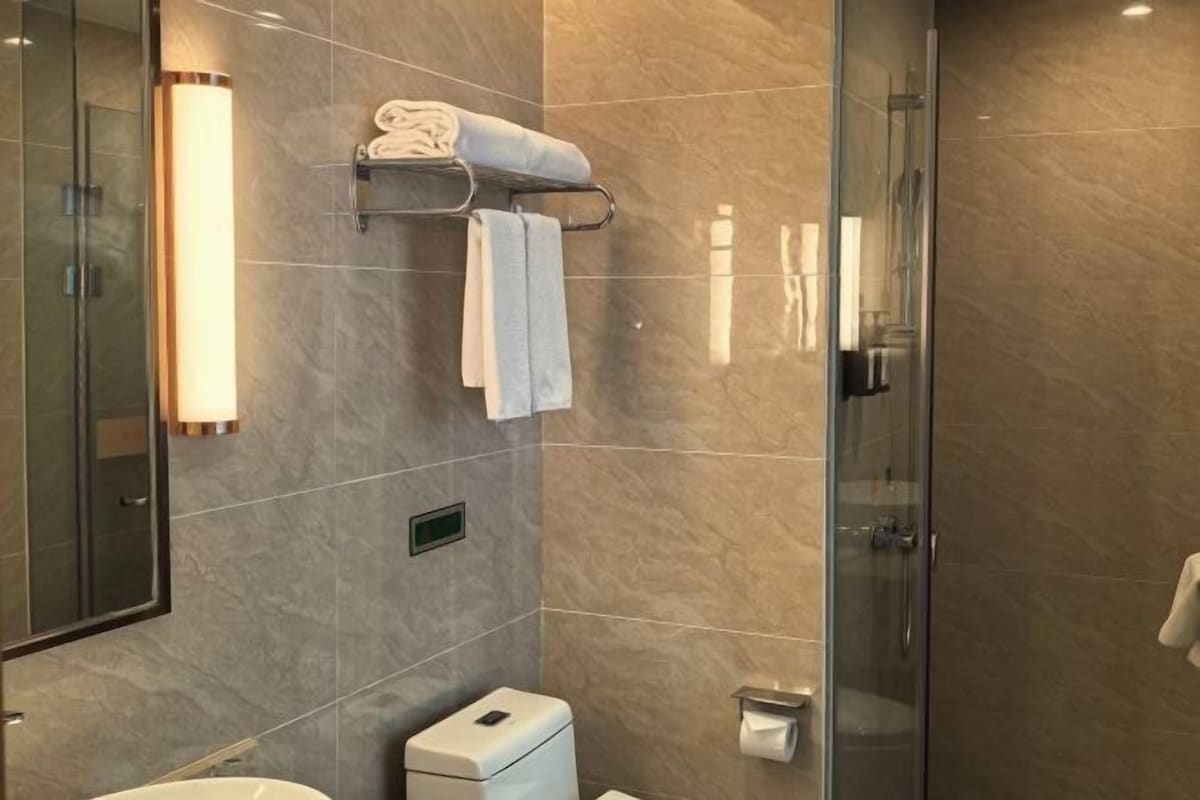 A modern bathroom with a glass shower enclosure, a toilet, and a towel rack with towels.