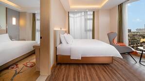 Ein Hotelzimmer mit einem großen Bett, einem Sessel, einem Schreibtisch und Blick auf die Stadt.