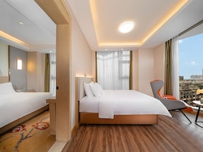 A hotel room with a large bed, a chair, a desk, and a view of the city. - Vienna International Hotel (Chengdu)