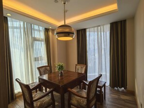 A dining area with a wooden table and chairs, a hanging light fixture, and large windows with curtains. - Vienna International Hotel (Chengdu)