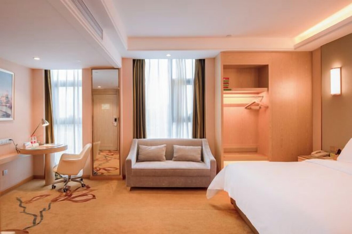A hotel room with a bed, a sofa, a desk with a chair, a vanity with a mirror, and a shower area.